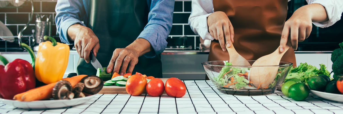two people cutting fresh veggies and fruit